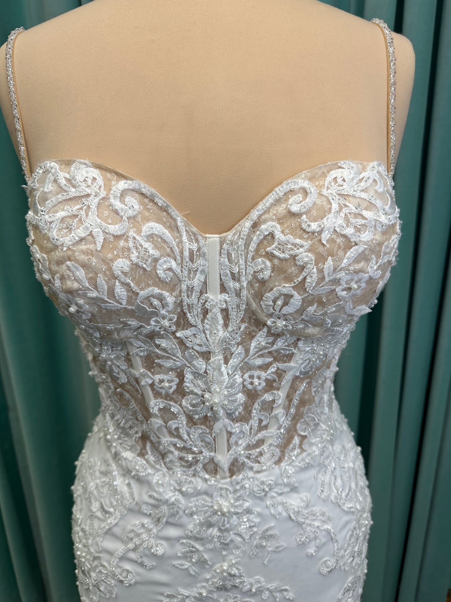 Liena ivory spaghetti strap wedding dress on mannequin with illusion corset bodice, floral lace appliqués, sweetheart neckline, and crepe skirt.
