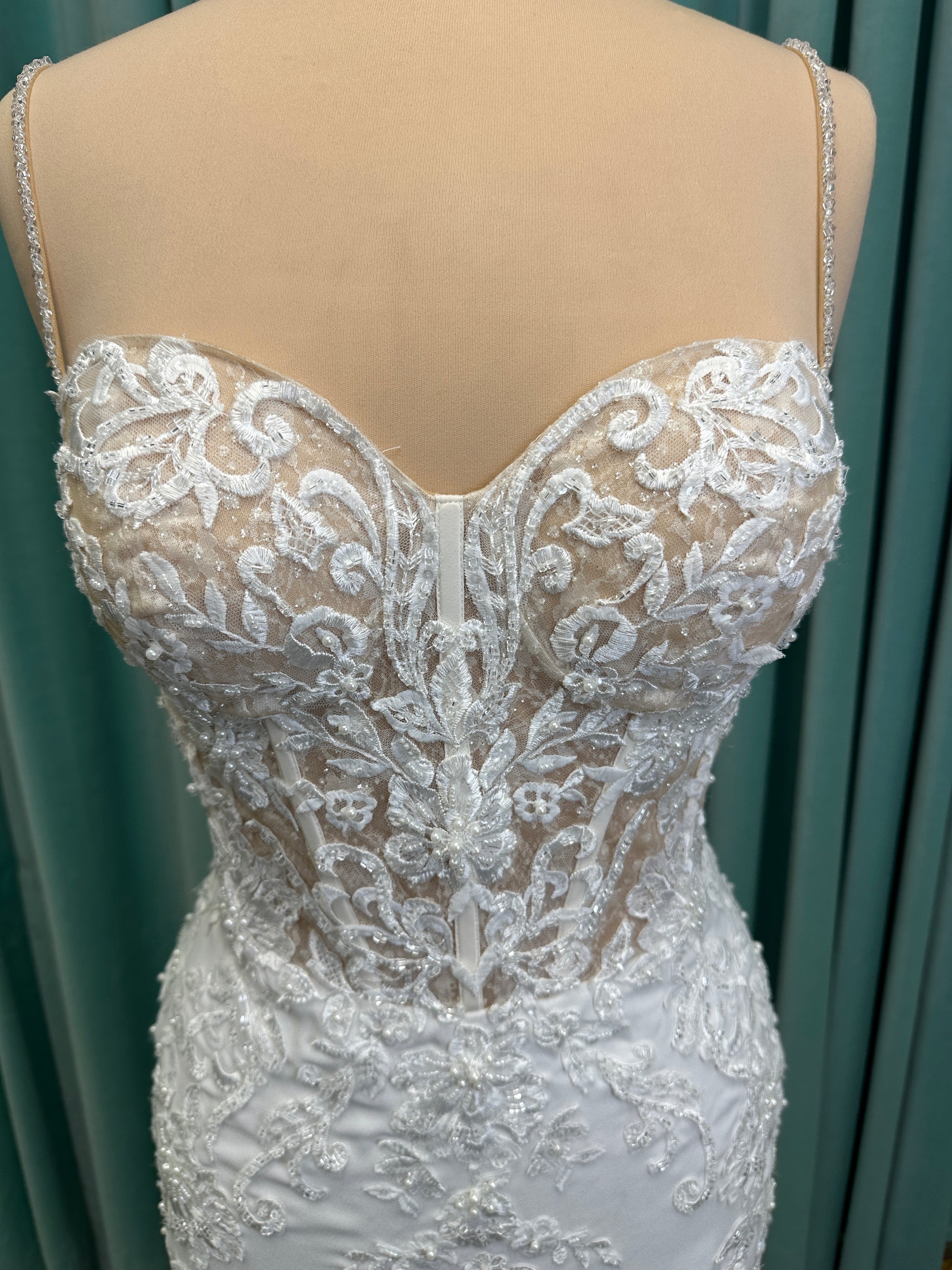 Liena ivory spaghetti strap wedding dress on mannequin with illusion corset bodice, floral lace appliqués, sweetheart neckline, and crepe skirt.
