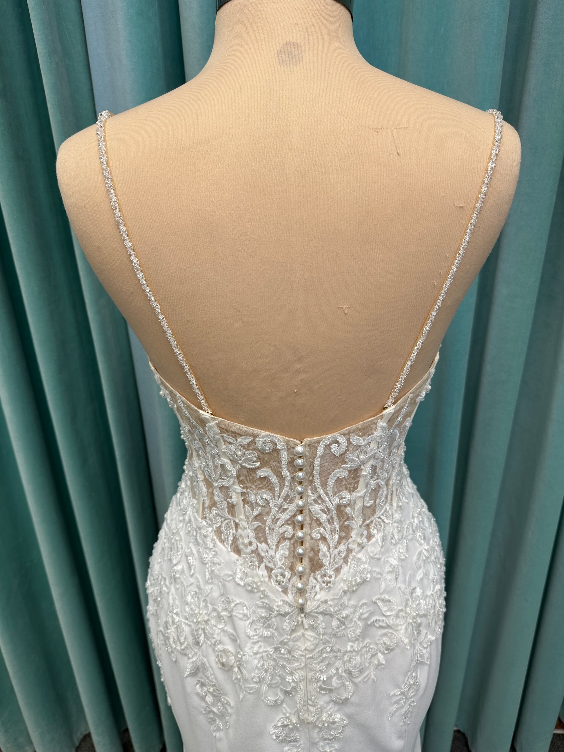 Liena ivory spaghetti strap wedding dress on mannequin with illusion corset bodice, floral lace appliqués, sweetheart neckline, and crepe skirt.
