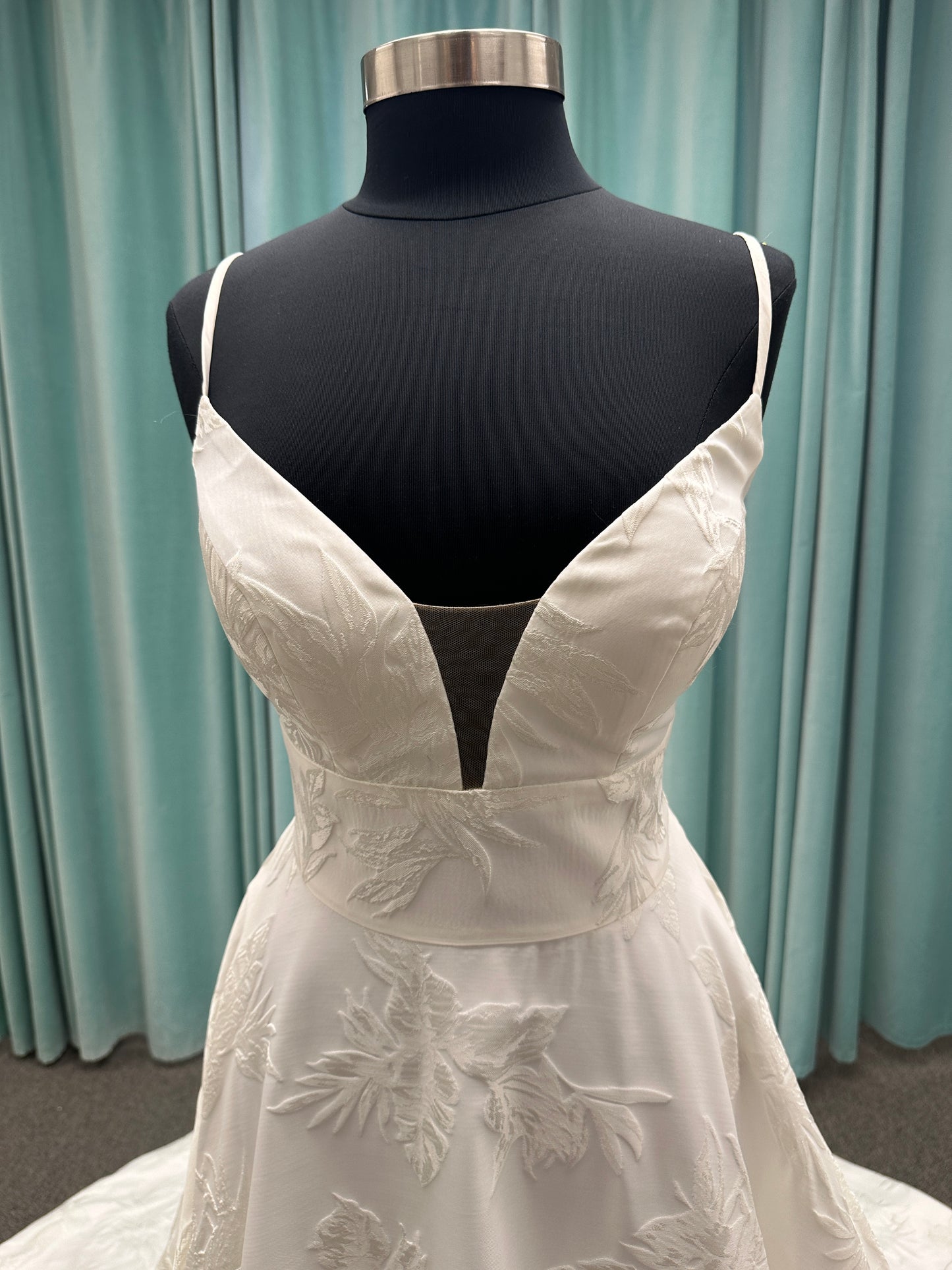Lisha ivory spaghetti strap V-neck ballgown wedding dress on mannequin in floral jacquard fabric with a full sweeping skirt.
