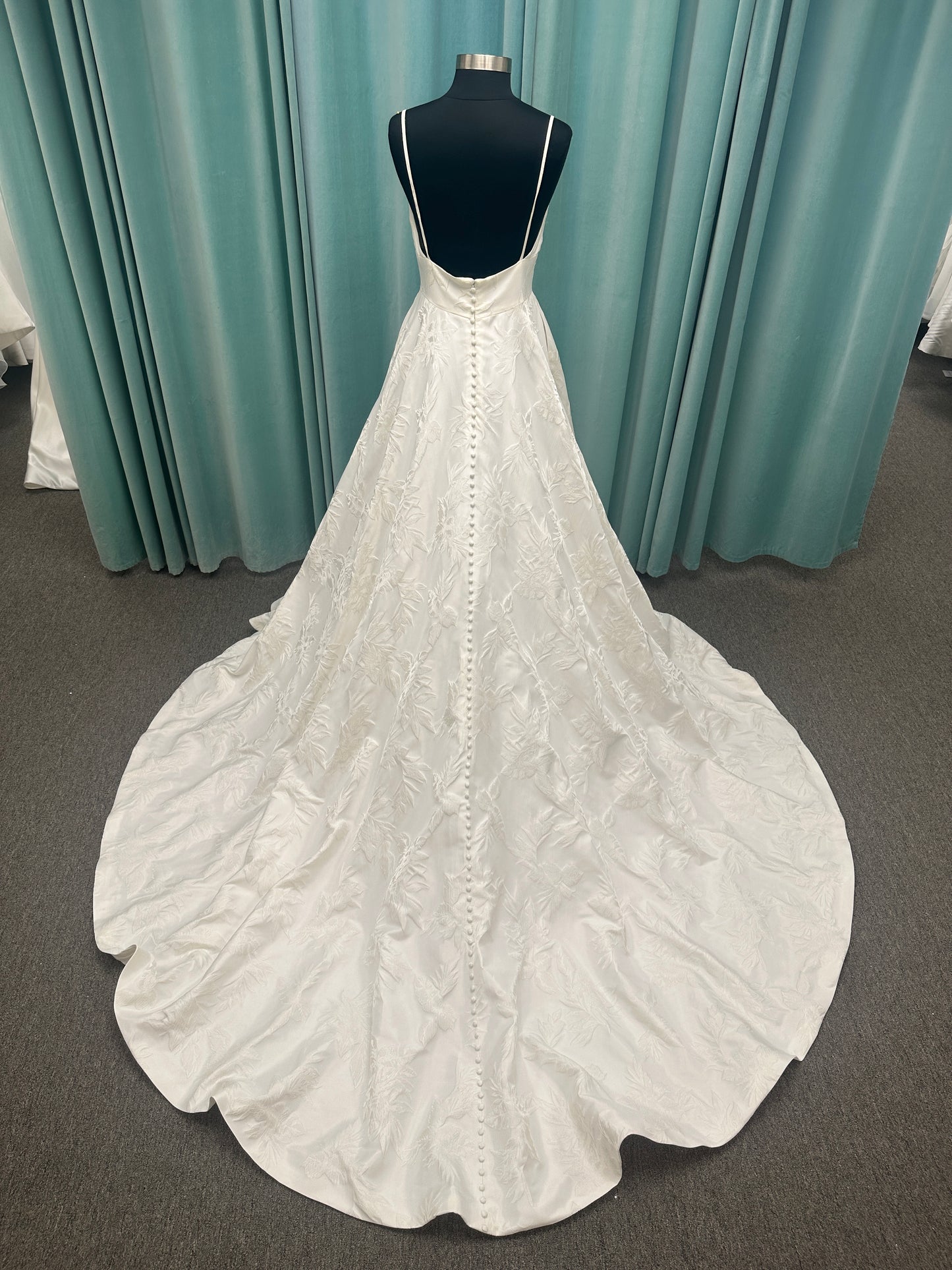 Lisha ivory spaghetti strap V-neck ballgown wedding dress on mannequin in floral jacquard fabric with a full sweeping skirt.
