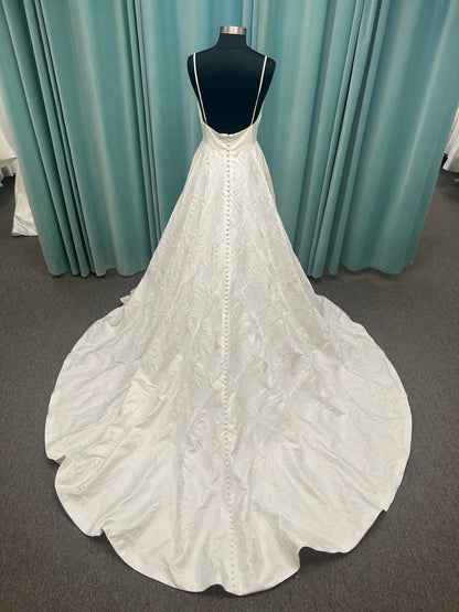 Lisha ivory spaghetti strap V-neck ballgown wedding dress on mannequin in floral jacquard fabric with a full sweeping skirt.
