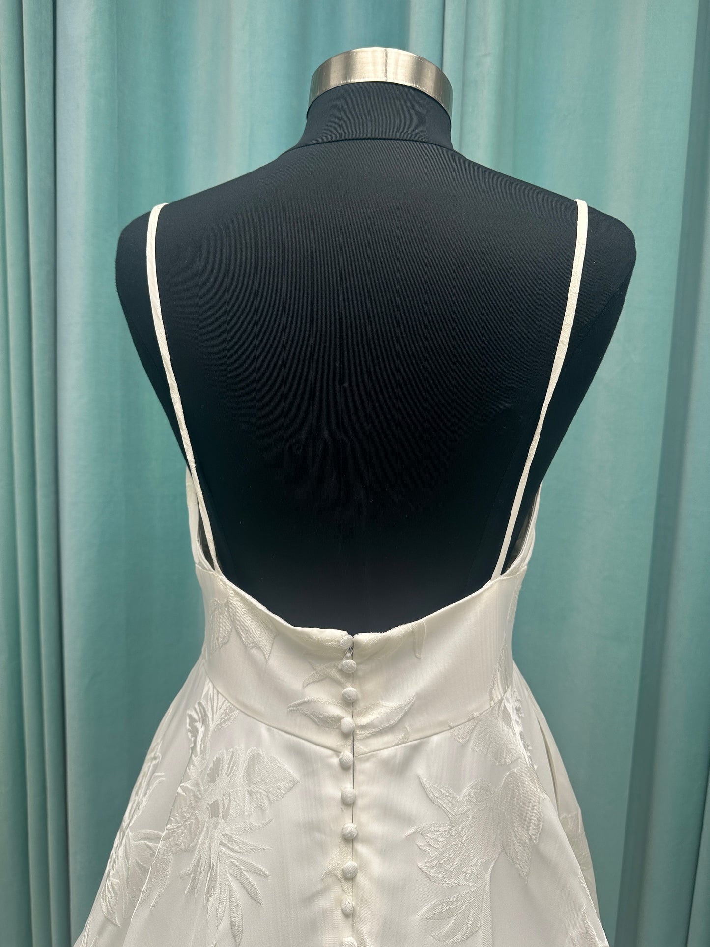 Lisha ivory spaghetti strap V-neck ballgown wedding dress on mannequin in floral jacquard fabric with a full sweeping skirt.
