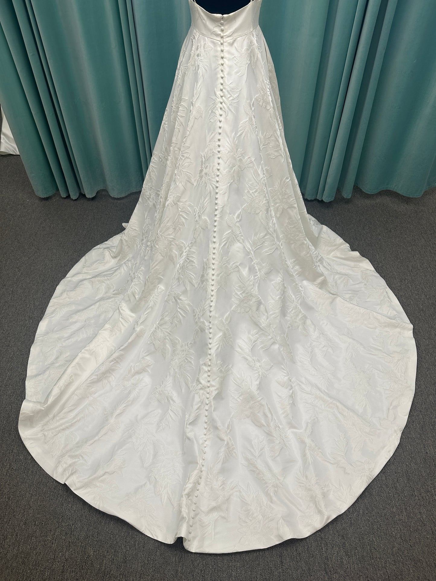 Lisha ivory spaghetti strap V-neck ballgown wedding dress on mannequin in floral jacquard fabric with a full sweeping skirt.
