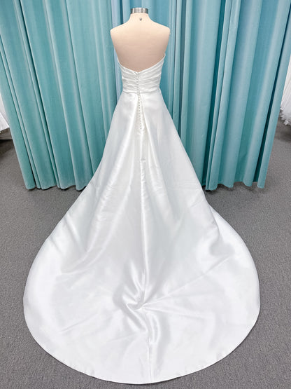 Moonlight Bridal J6978 Livana A-line wedding dress on mannequin with strapless scoop neckline, ruched mikado bodice, asymmetrical draped waist, high front slit, and chapel train