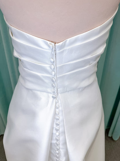 Moonlight Bridal J6978 Livana A-line wedding dress on mannequin with strapless scoop neckline, ruched mikado bodice, asymmetrical draped waist, high front slit, and chapel train