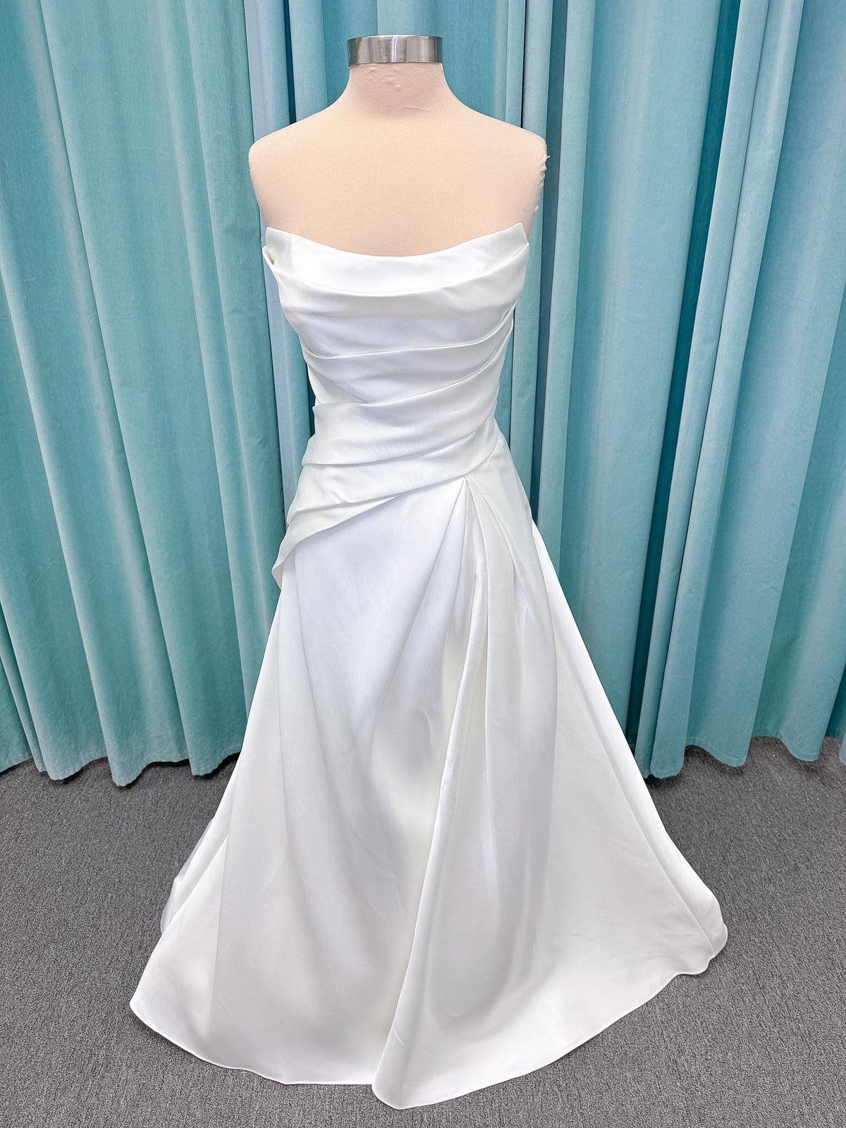 Moonlight Bridal J6978 Livana A-line wedding dress on mannequin with strapless scoop neckline, ruched mikado bodice, asymmetrical draped waist, high front slit, and chapel train