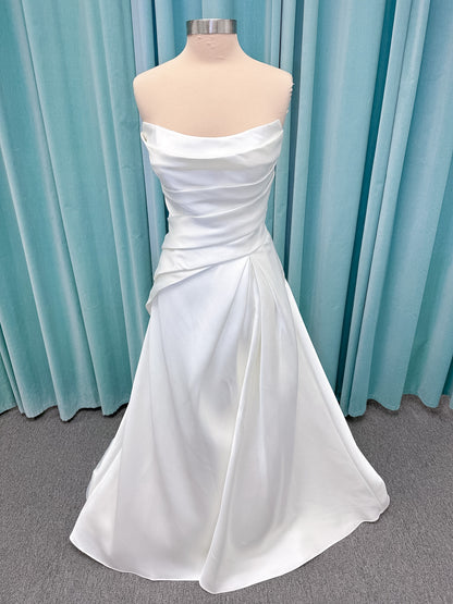Moonlight Bridal J6978 Livana A-line wedding dress on mannequin with strapless scoop neckline, ruched mikado bodice, asymmetrical draped waist, high front slit, and chapel train