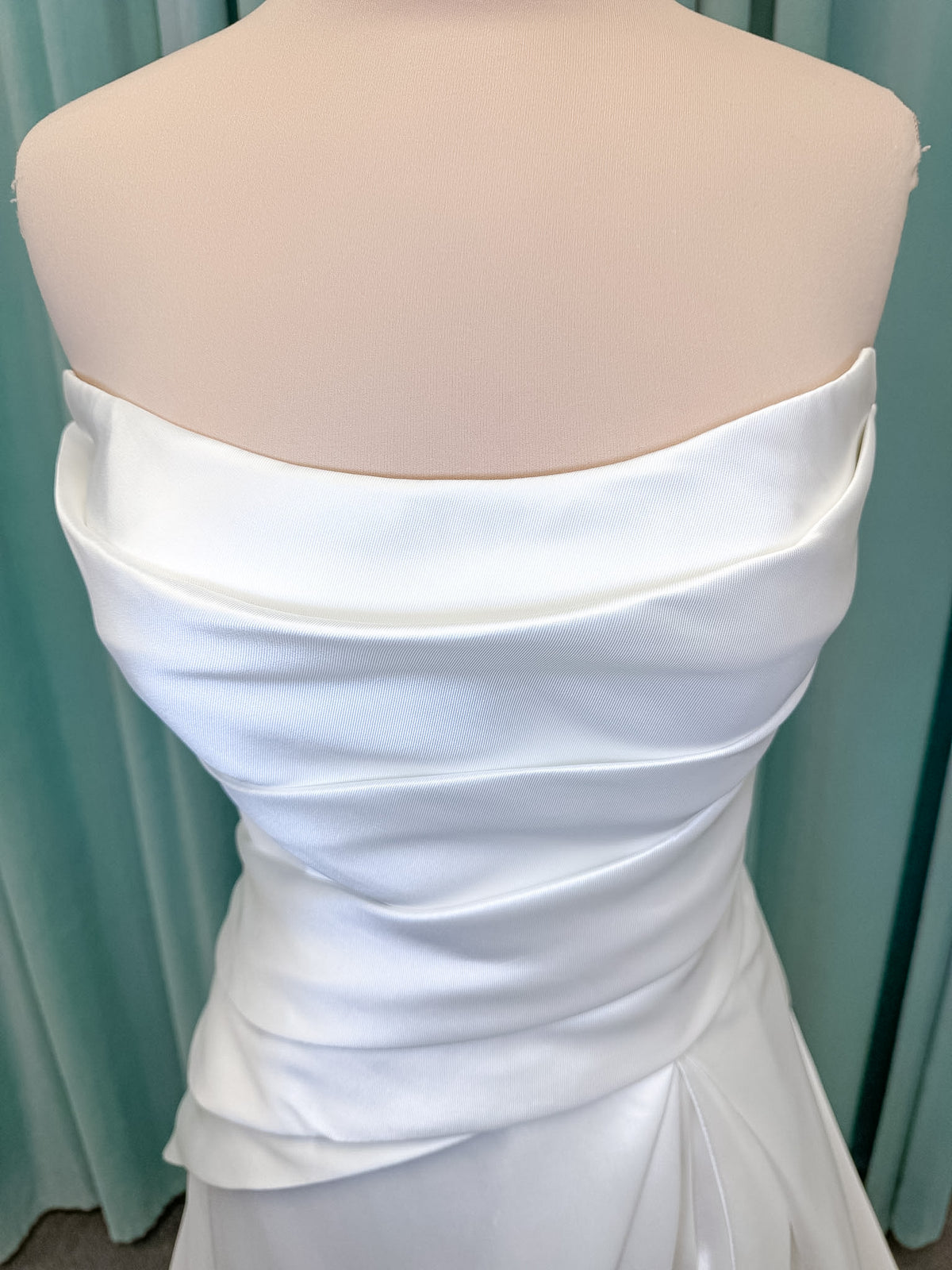 Moonlight Bridal J6978 Livana A-line wedding dress on mannequin with strapless scoop neckline, ruched mikado bodice, asymmetrical draped waist, high front slit, and chapel train
