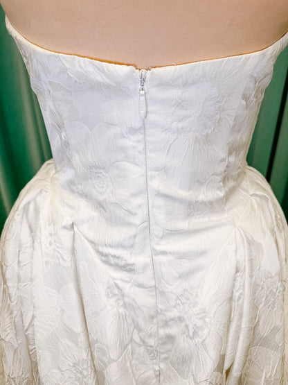 Haley Mai Bridal Lorea ballgown wedding dress on mannequin with strapless scoop neckline, seamed basque waist bodice, pleated ivory floral jacquard skirt, and long train
