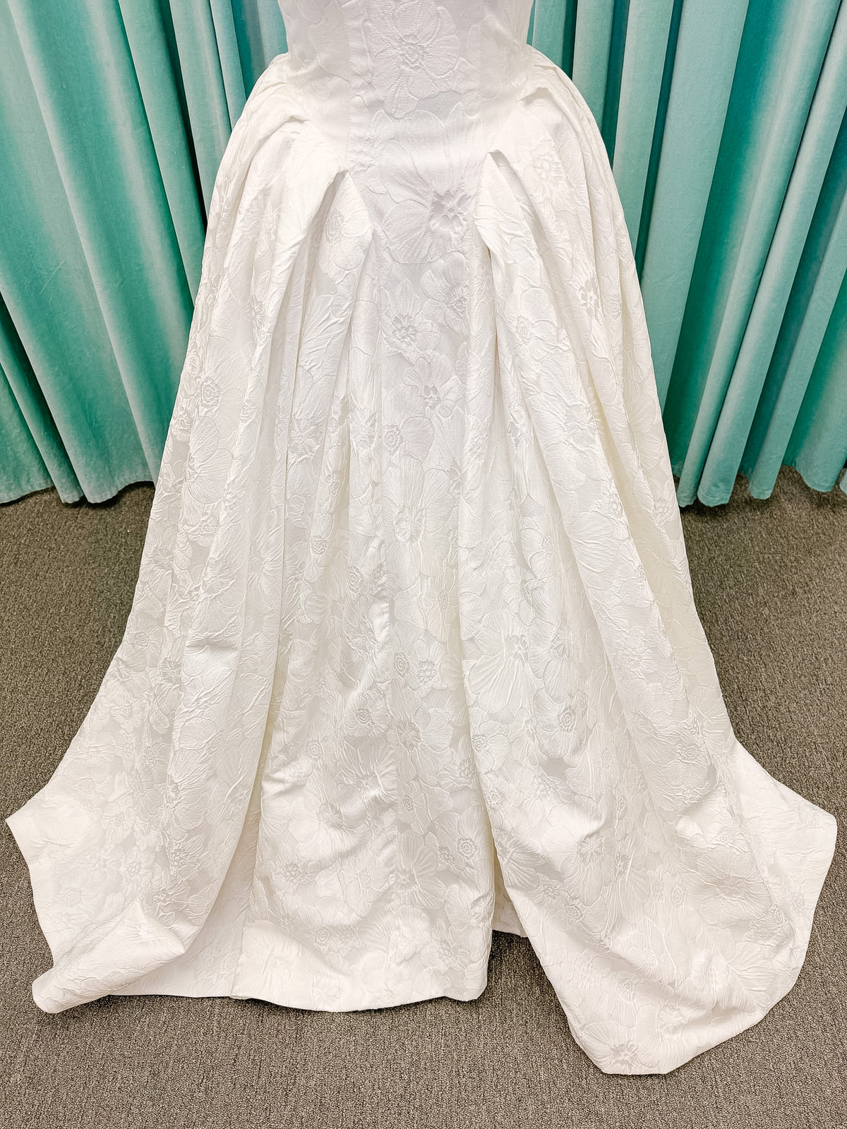 Haley Mai Bridal Lorea ballgown wedding dress on mannequin with strapless scoop neckline, seamed basque waist bodice, pleated ivory floral jacquard skirt, and long train