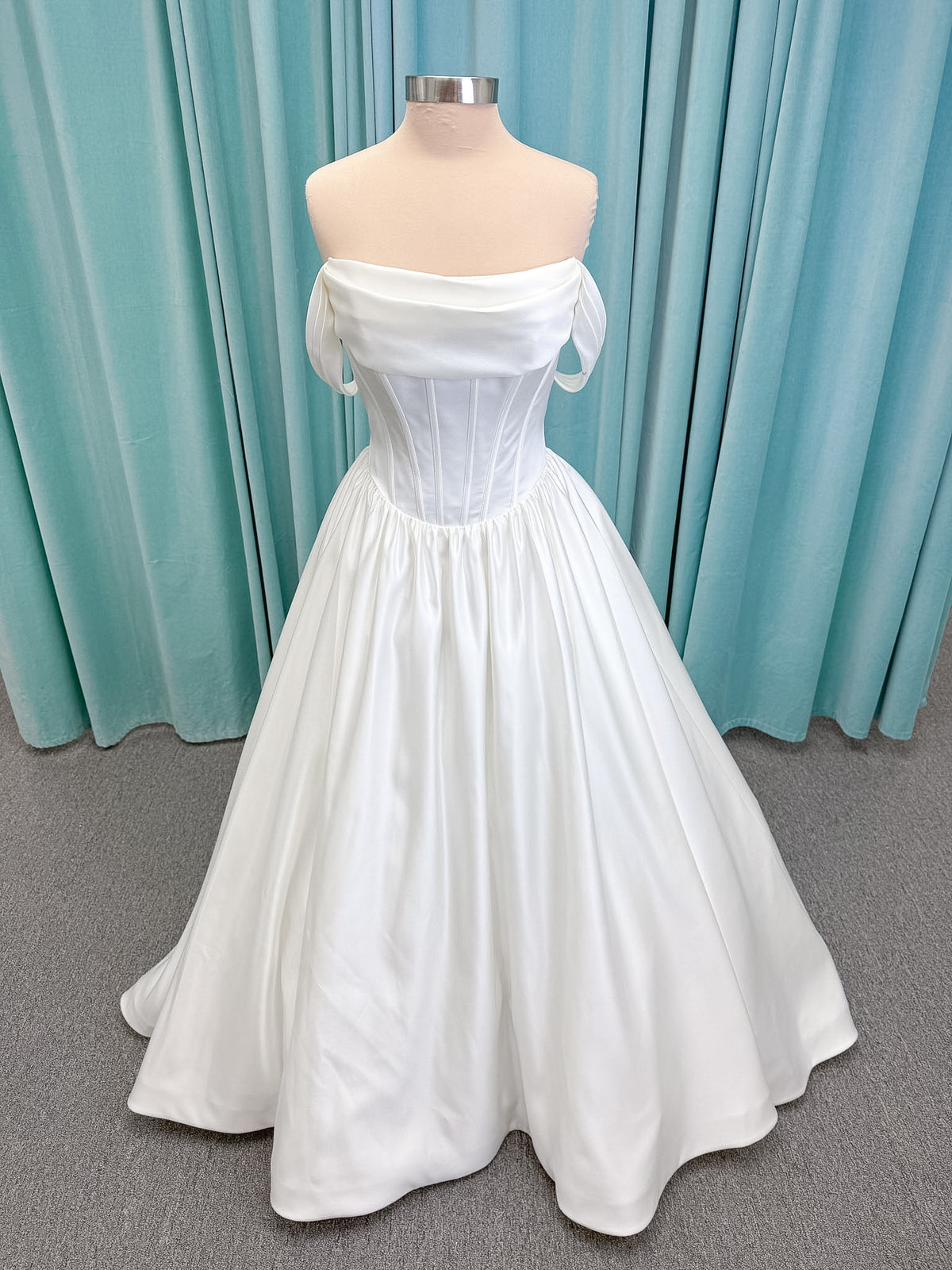 Moonlight Bridal J6953 Luna A-line wedding dress on mannequin with straight draped satin neckline, pleated off-the-shoulder swag sleeves, boned basque waist, full rouched satin skirt, and sweep train
