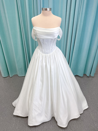 Moonlight Bridal J6953 Luna A-line wedding dress on mannequin with straight draped satin neckline, pleated off-the-shoulder swag sleeves, boned basque waist, full rouched satin skirt, and sweep train