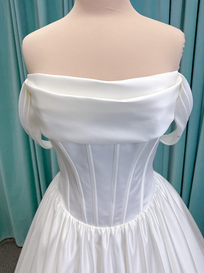 Moonlight Bridal J6953 Luna A-line wedding dress on mannequin with straight draped satin neckline, pleated off-the-shoulder swag sleeves, boned basque waist, full rouched satin skirt, and sweep train