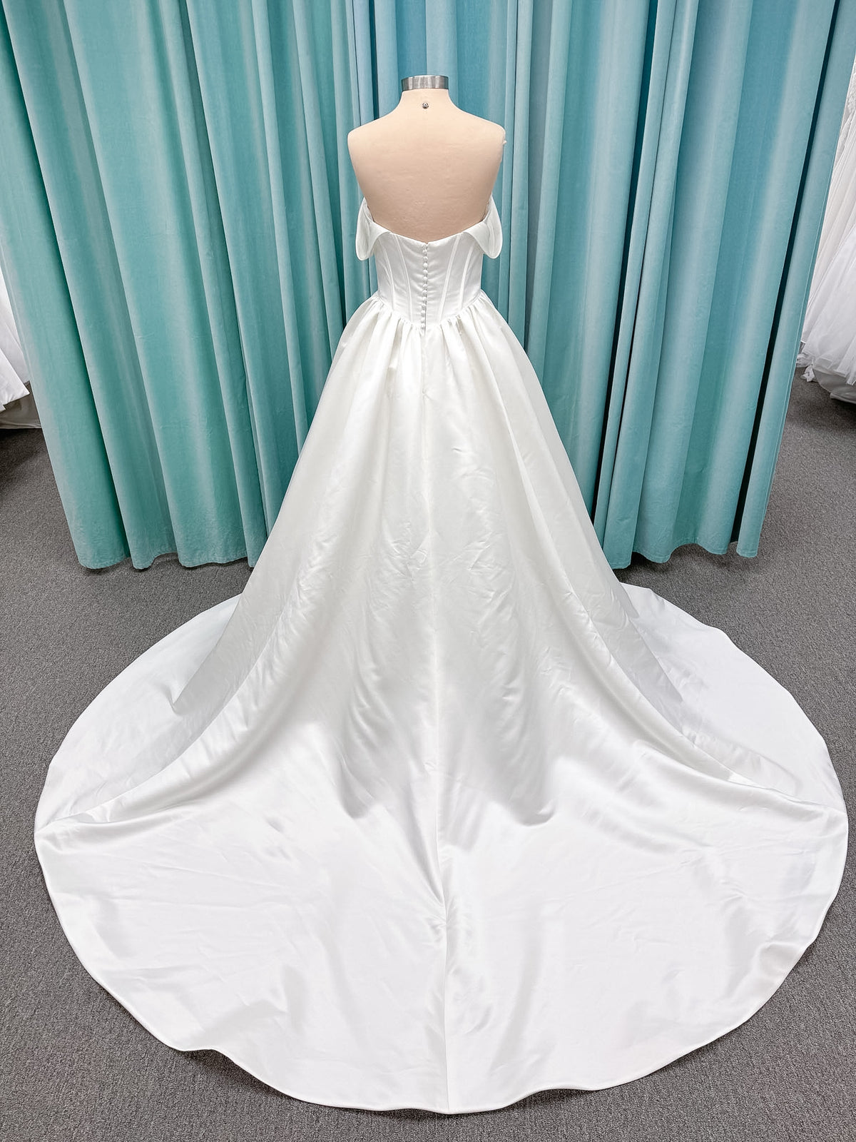 Moonlight Bridal J6953 Luna A-line wedding dress on mannequin with straight draped satin neckline, pleated off-the-shoulder swag sleeves, boned basque waist, full rouched satin skirt, and sweep train
