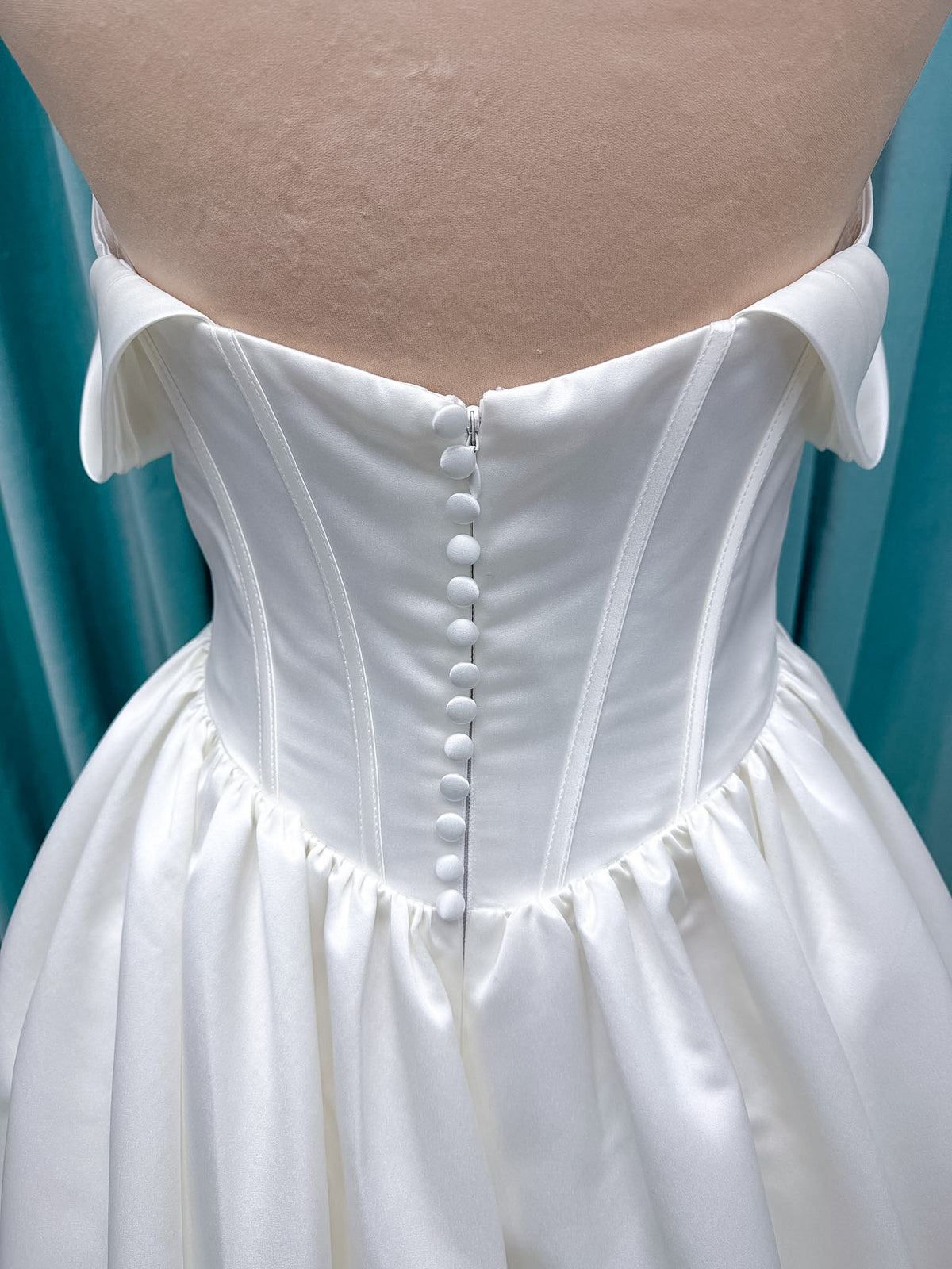 Moonlight Bridal J6953 Luna A-line wedding dress on mannequin with straight draped satin neckline, pleated off-the-shoulder swag sleeves, boned basque waist, full rouched satin skirt, and sweep train