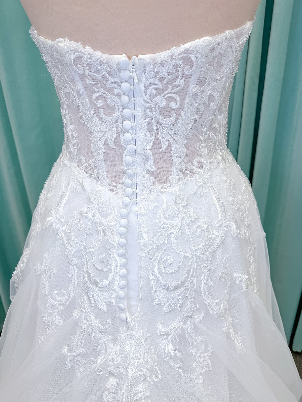 Moonlight Bridal J6972 Lunetta A-line wedding dress on mannequin with strapless soft sweetheart neckline, beaded lace appliques over tulle and Chantilly lace, drop waist, and scalloped applique sweep train