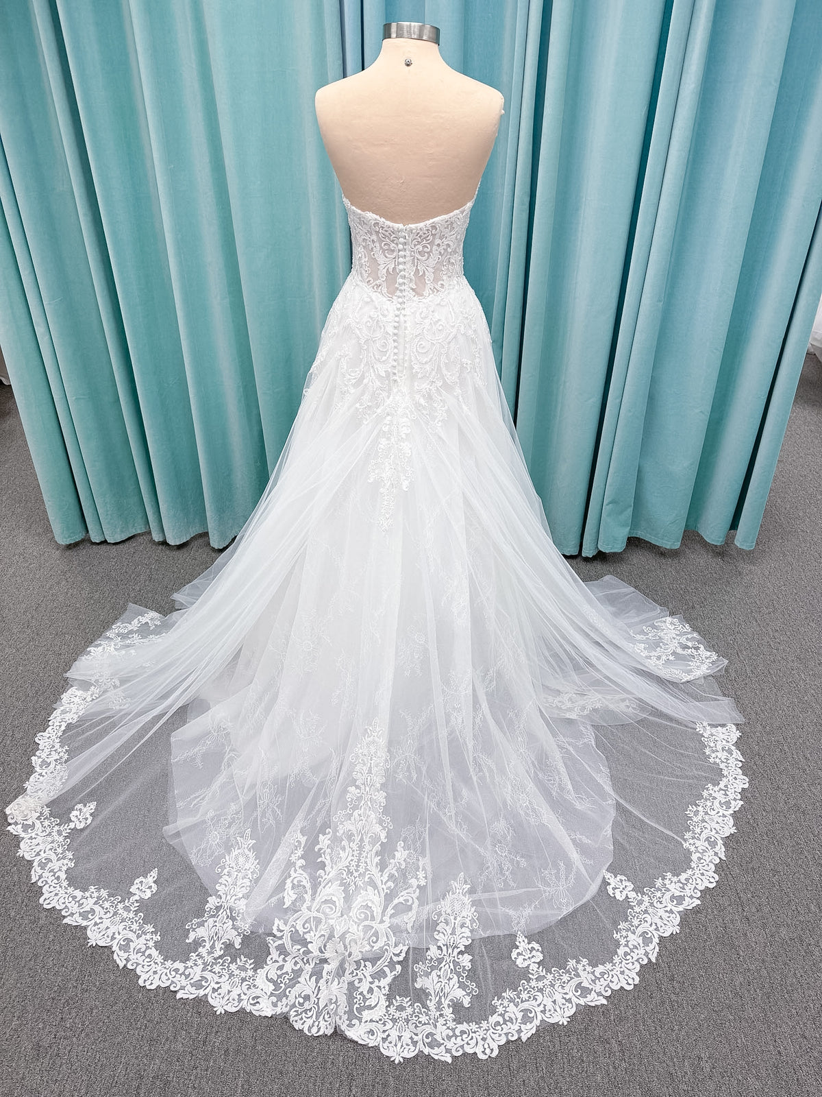 Moonlight Bridal J6972 Lunetta A-line wedding dress on mannequin with strapless soft sweetheart neckline, beaded lace appliques over tulle and Chantilly lace, drop waist, and scalloped applique sweep train