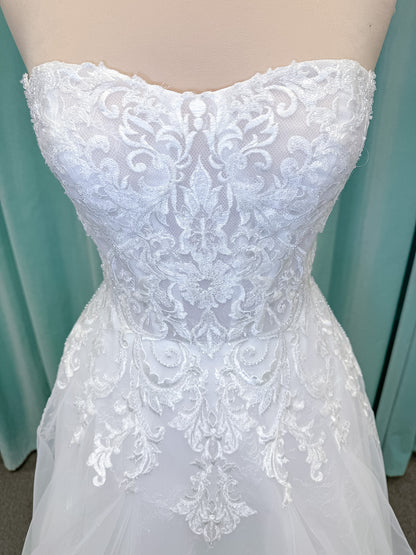 Moonlight Bridal J6972 Lunetta A-line wedding dress on mannequin with strapless soft sweetheart neckline, beaded lace appliques over tulle and Chantilly lace, drop waist, and scalloped applique sweep train