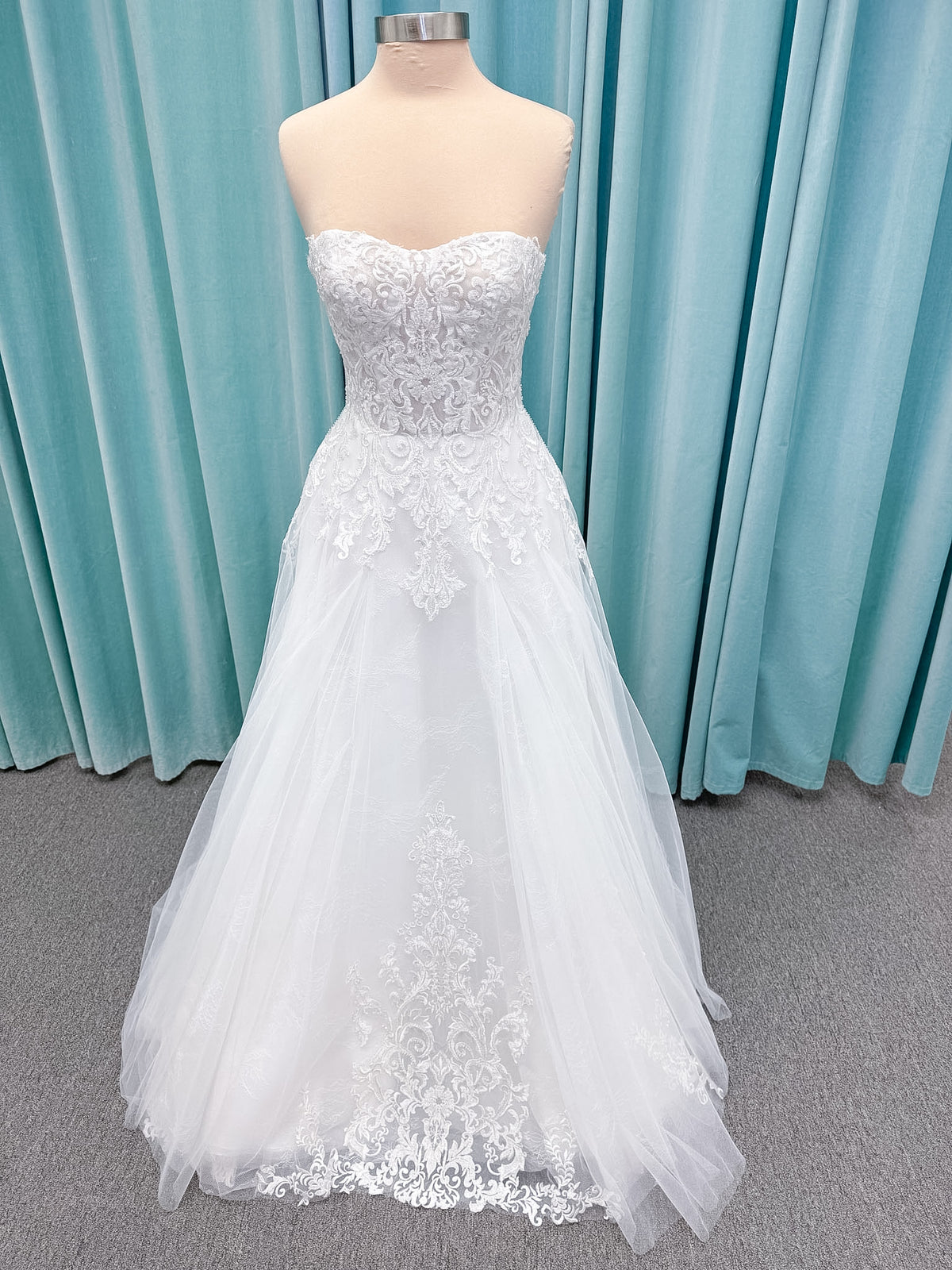 Moonlight Bridal J6972 Lunetta A-line wedding dress on mannequin with strapless soft sweetheart neckline, beaded lace appliques over tulle and Chantilly lace, drop waist, and scalloped applique sweep train