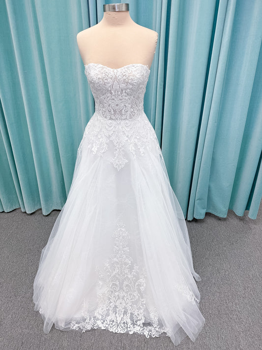 Moonlight Bridal J6972 Lunetta A-line wedding dress on mannequin with strapless soft sweetheart neckline, beaded lace appliques over tulle and Chantilly lace, drop waist, and scalloped applique sweep train