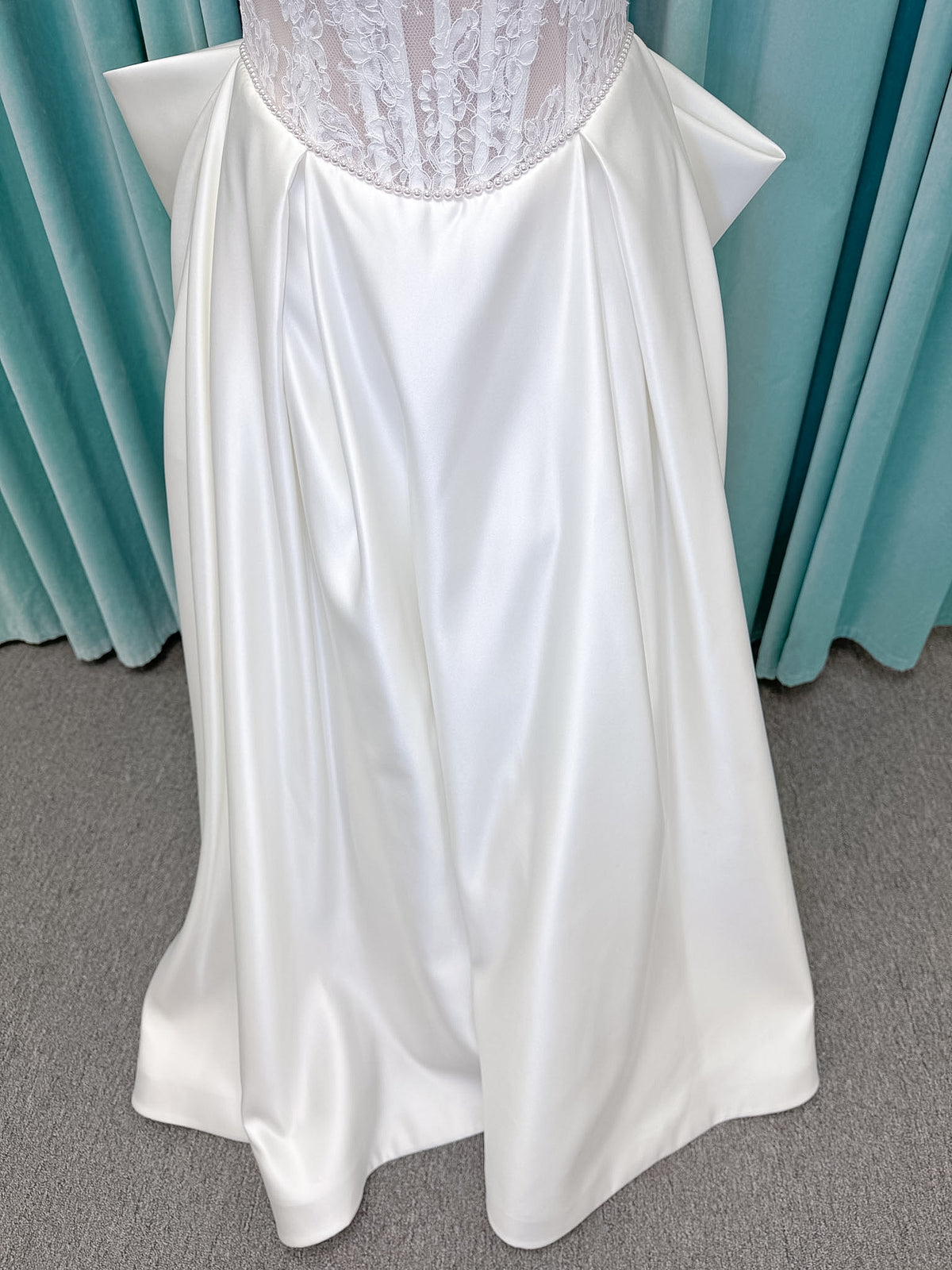 Moonlight Bridal J6998 Lusine A-line wedding dress on mannequin with strapless illusion scoop neckline, corded lace bodice with exposed boning, pearl-trimmed basque waist, full satin skirt with pockets, half lace-up back, and chapel train
