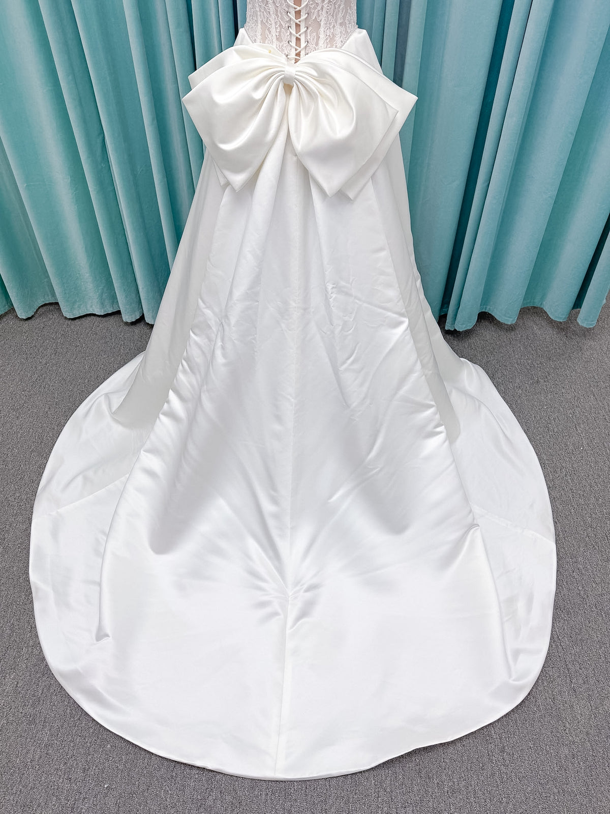 Moonlight Bridal J6998 Lusine A-line wedding dress on mannequin with strapless illusion scoop neckline, corded lace bodice with exposed boning, pearl-trimmed basque waist, full satin skirt with pockets, half lace-up back, and chapel train