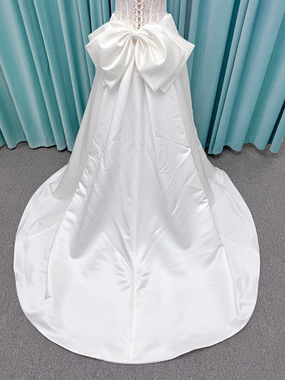 Moonlight Bridal J6998 Lusine A-line wedding dress on mannequin with strapless illusion scoop neckline, corded lace bodice with exposed boning, pearl-trimmed basque waist, full satin skirt with pockets, half lace-up back, and chapel train