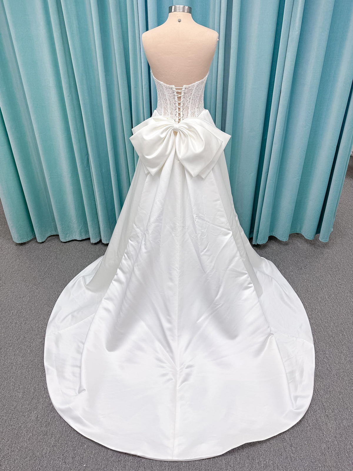 Moonlight Bridal J6998 Lusine A-line wedding dress on mannequin with strapless illusion scoop neckline, corded lace bodice with exposed boning, pearl-trimmed basque waist, full satin skirt with pockets, half lace-up back, and chapel train