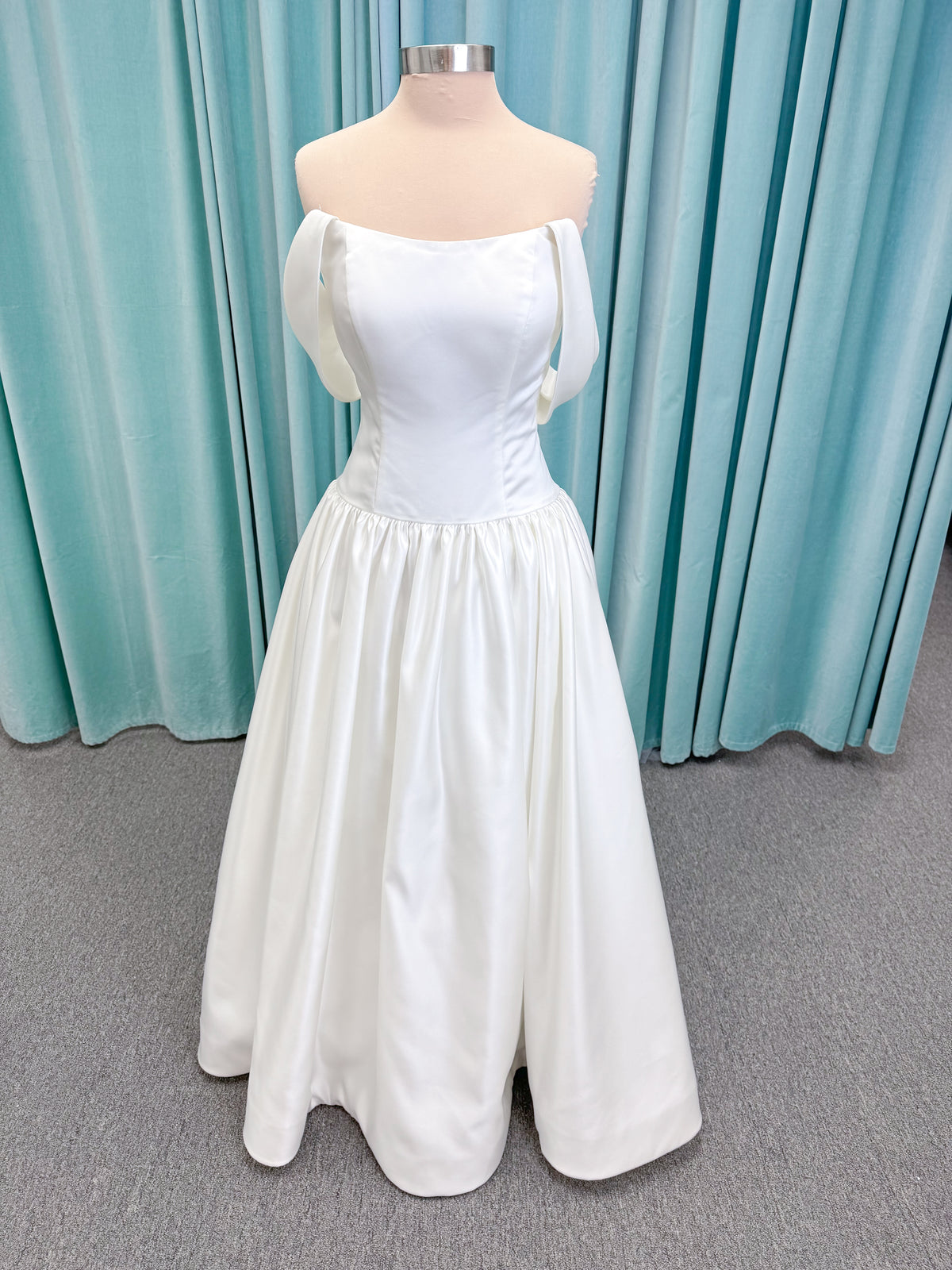 Moonlight Bridal J6956 Mahina ballgown wedding dress on mannequin with scoop neckline, detachable off-the-shoulder swag sleeves, drop waist, ruched shimmering satin skirt, and chapel train with horsehair hem