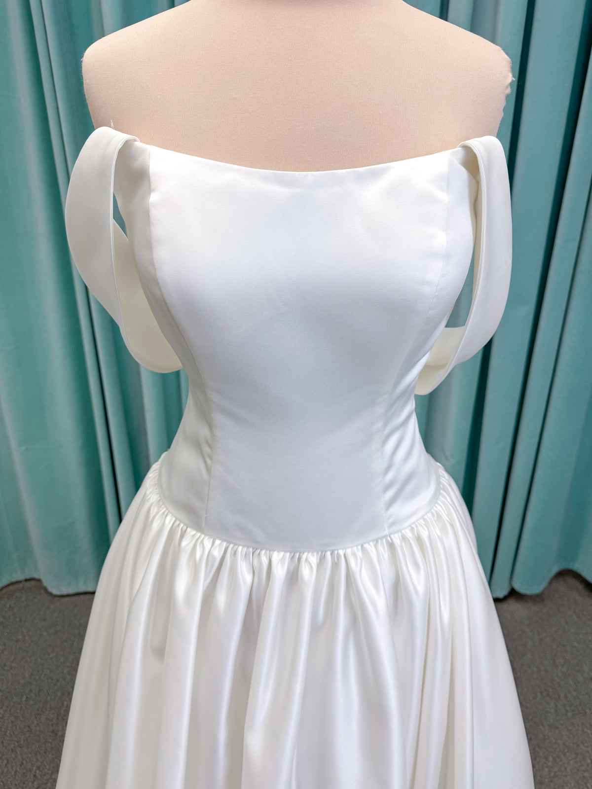 Moonlight Bridal J6956 Mahina ballgown wedding dress on mannequin with scoop neckline, detachable off-the-shoulder swag sleeves, drop waist, ruched shimmering satin skirt, and chapel train with horsehair hem