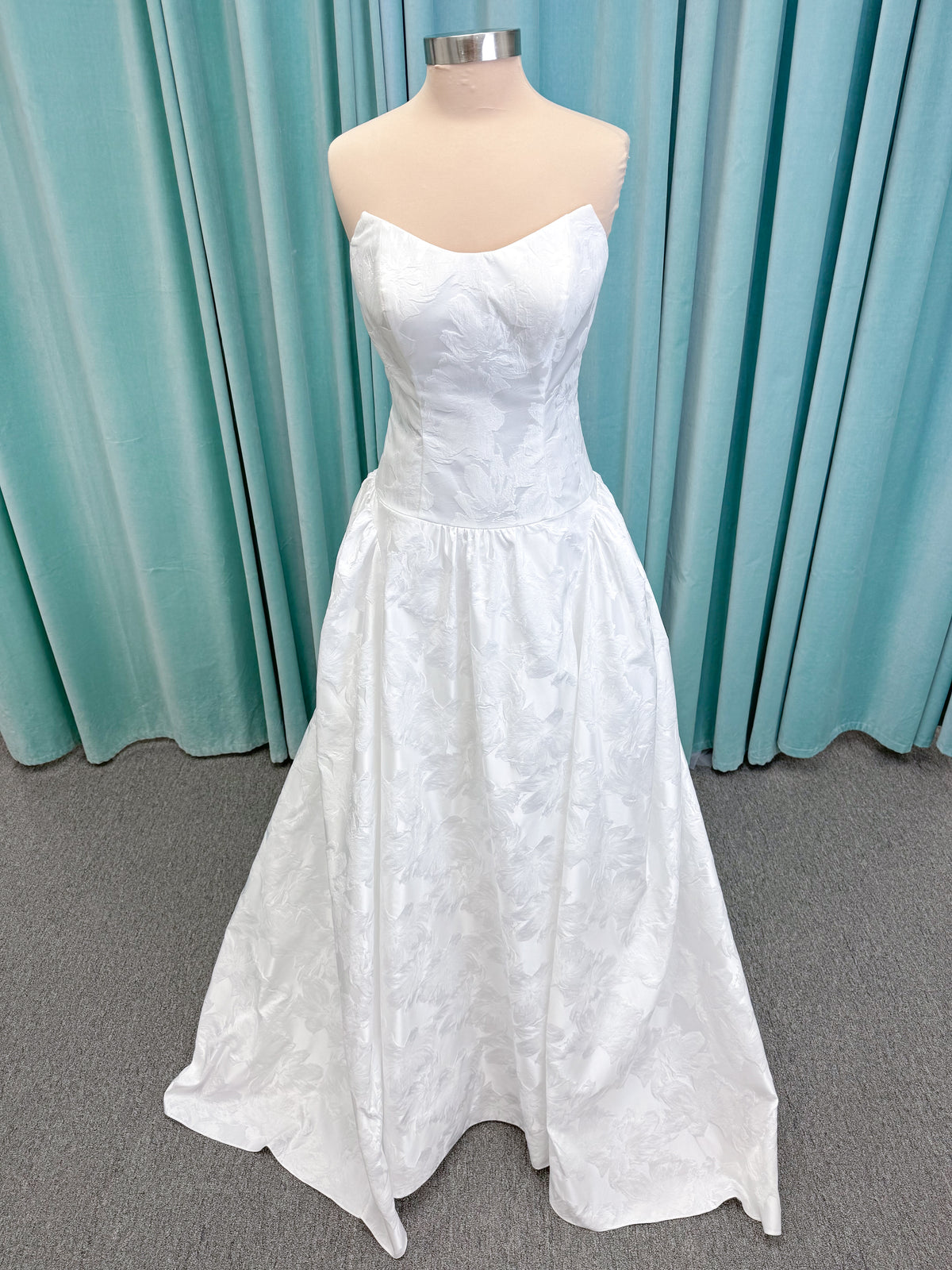 Moonlight Bridal J6994 Marama ballgown wedding dress on mannequin with strapless scoop neckline, textured satin jacquard, fitted drop-waist bodice, detachable short bow sleeves, full skirt, and sweep train