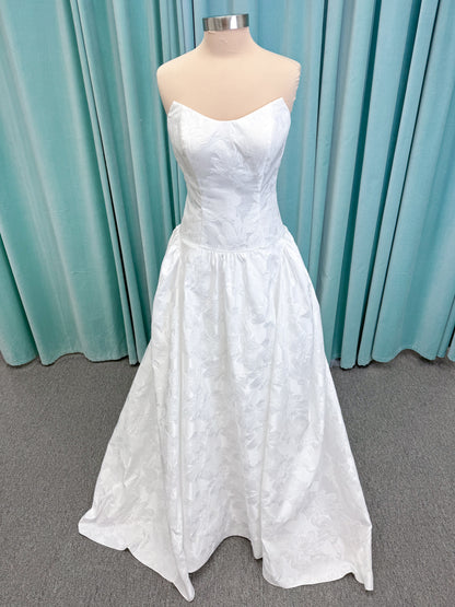 Moonlight Bridal J6994 Marama ballgown wedding dress on mannequin with strapless scoop neckline, textured satin jacquard, fitted drop-waist bodice, detachable short bow sleeves, full skirt, and sweep train