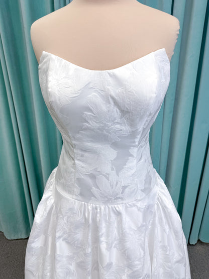 Moonlight Bridal J6994 Marama ballgown wedding dress on mannequin with strapless scoop neckline, textured satin jacquard, fitted drop-waist bodice, detachable short bow sleeves, full skirt, and sweep train