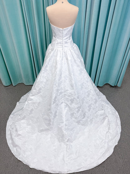 Moonlight Bridal J6994 Marama ballgown wedding dress on mannequin with strapless scoop neckline, textured satin jacquard, fitted drop-waist bodice, detachable short bow sleeves, full skirt, and sweep train