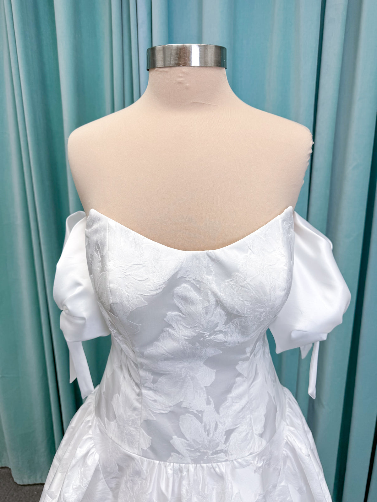 Moonlight Bridal J6994 Marama ballgown wedding dress on mannequin with strapless scoop neckline, textured satin jacquard, fitted drop-waist bodice, detachable short bow sleeves, full skirt, and sweep train
