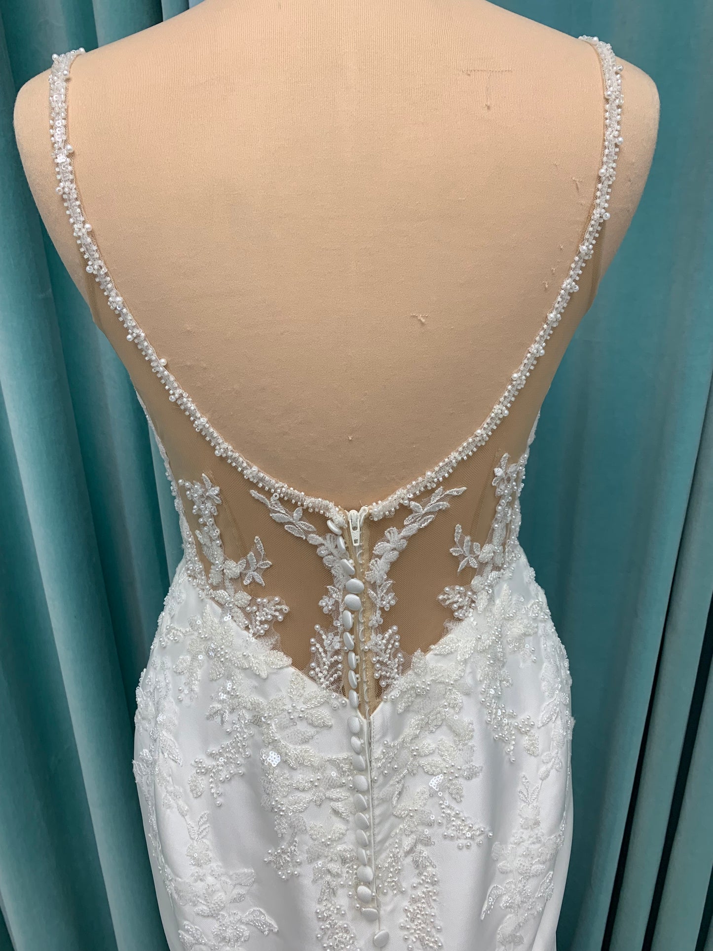Marjorie ivory spaghetti strap wedding dress on mannequin with illusion corset bodice, floral lace appliqués, and scoop neckline.
