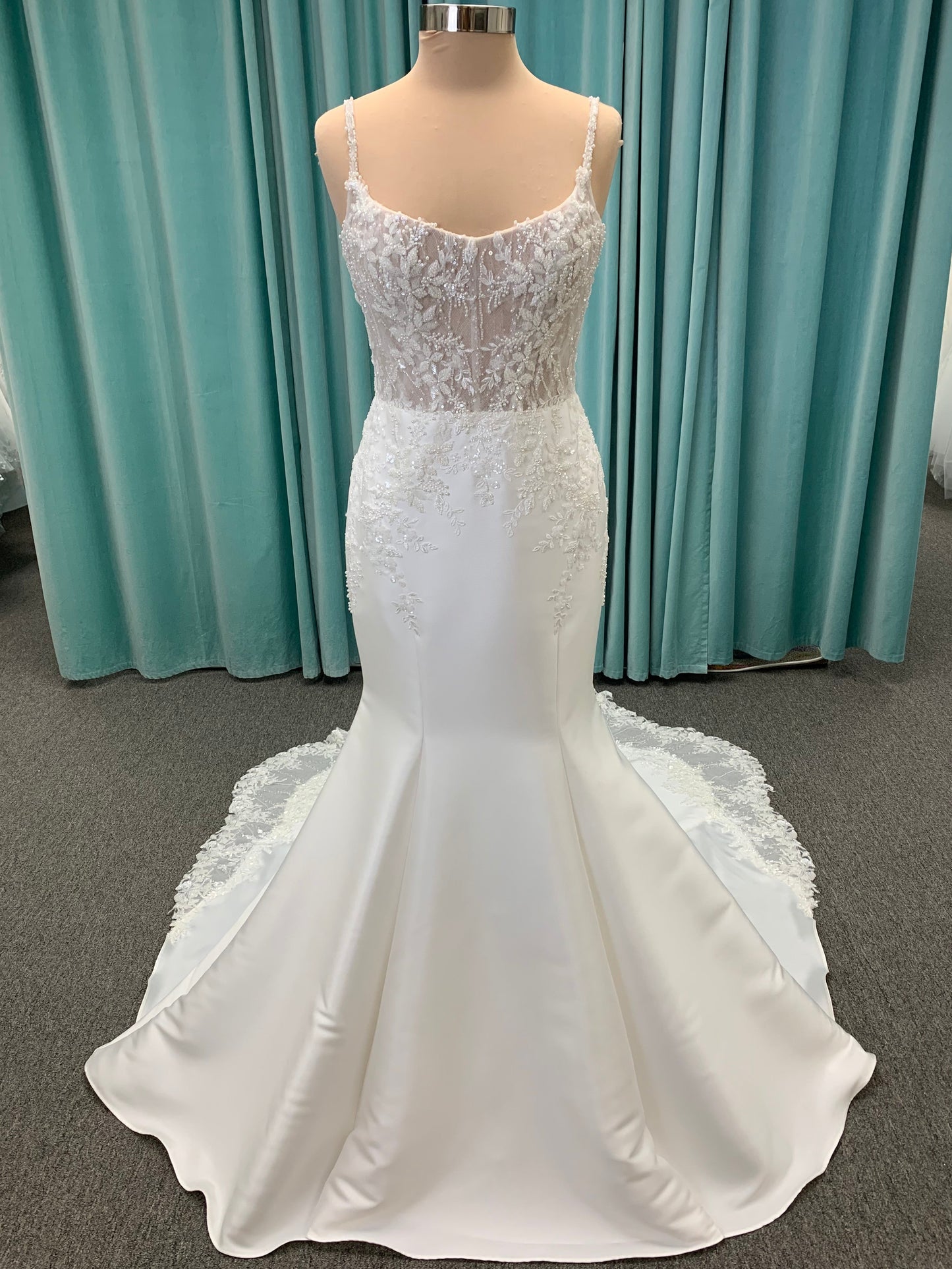 Marjorie ivory spaghetti strap wedding dress on mannequin with illusion corset bodice, floral lace appliqués, and scoop neckline.
