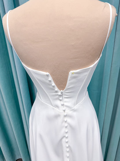 Crepe A-line wedding dress with spaghetti straps, draped V-neckline, ruched bodice, defined waist, and flowing skirt.