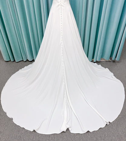 Crepe A-line wedding dress with spaghetti straps, draped V-neckline, ruched bodice, defined waist, and flowing skirt.