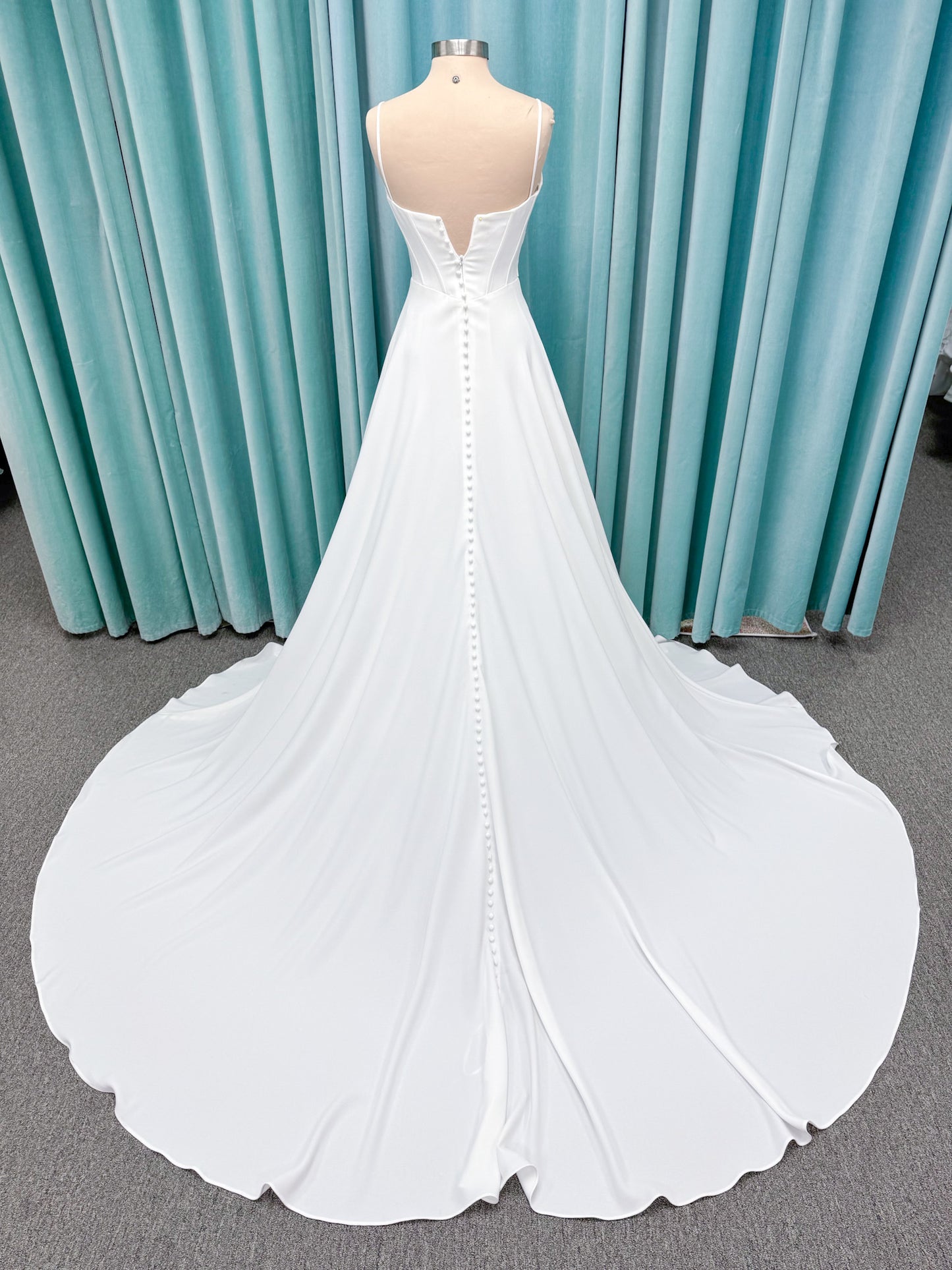 Crepe A-line wedding dress with spaghetti straps, draped V-neckline, ruched bodice, defined waist, and flowing skirt.