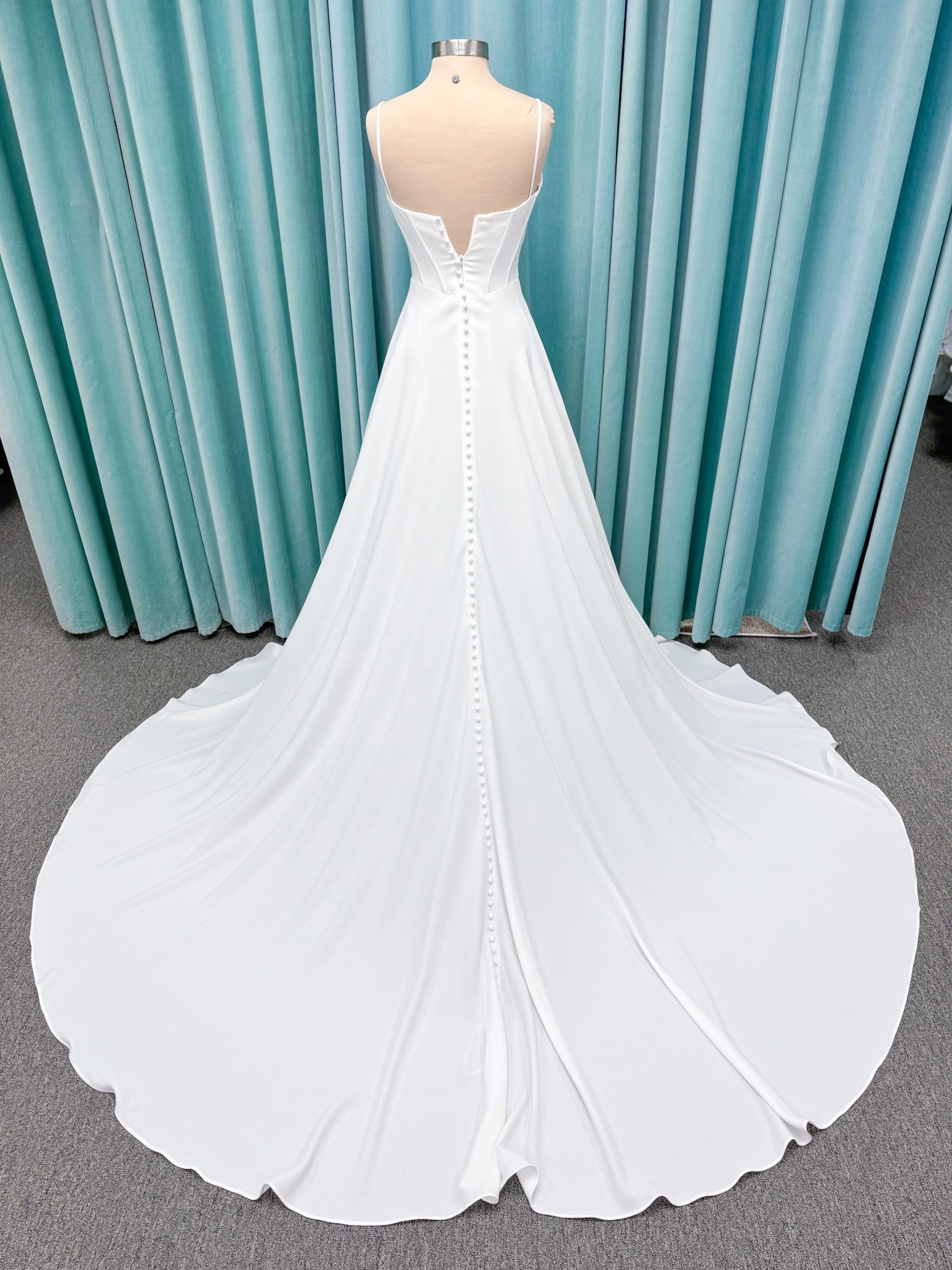 Crepe A-line wedding dress with spaghetti straps, draped V-neckline, ruched bodice, defined waist, and flowing skirt.