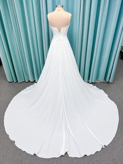 Crepe A-line wedding dress with spaghetti straps, draped V-neckline, ruched bodice, defined waist, and flowing skirt.