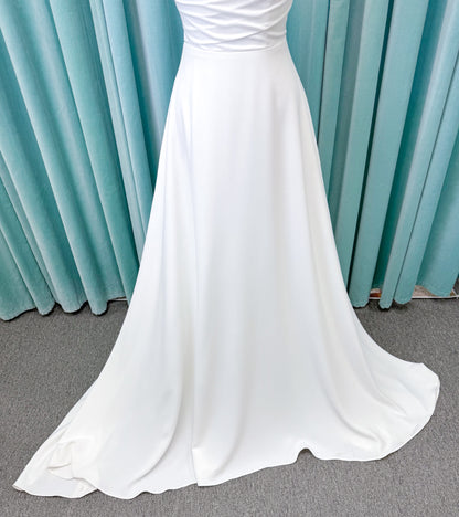 Crepe A-line wedding dress with spaghetti straps, draped V-neckline, ruched bodice, defined waist, and flowing skirt.