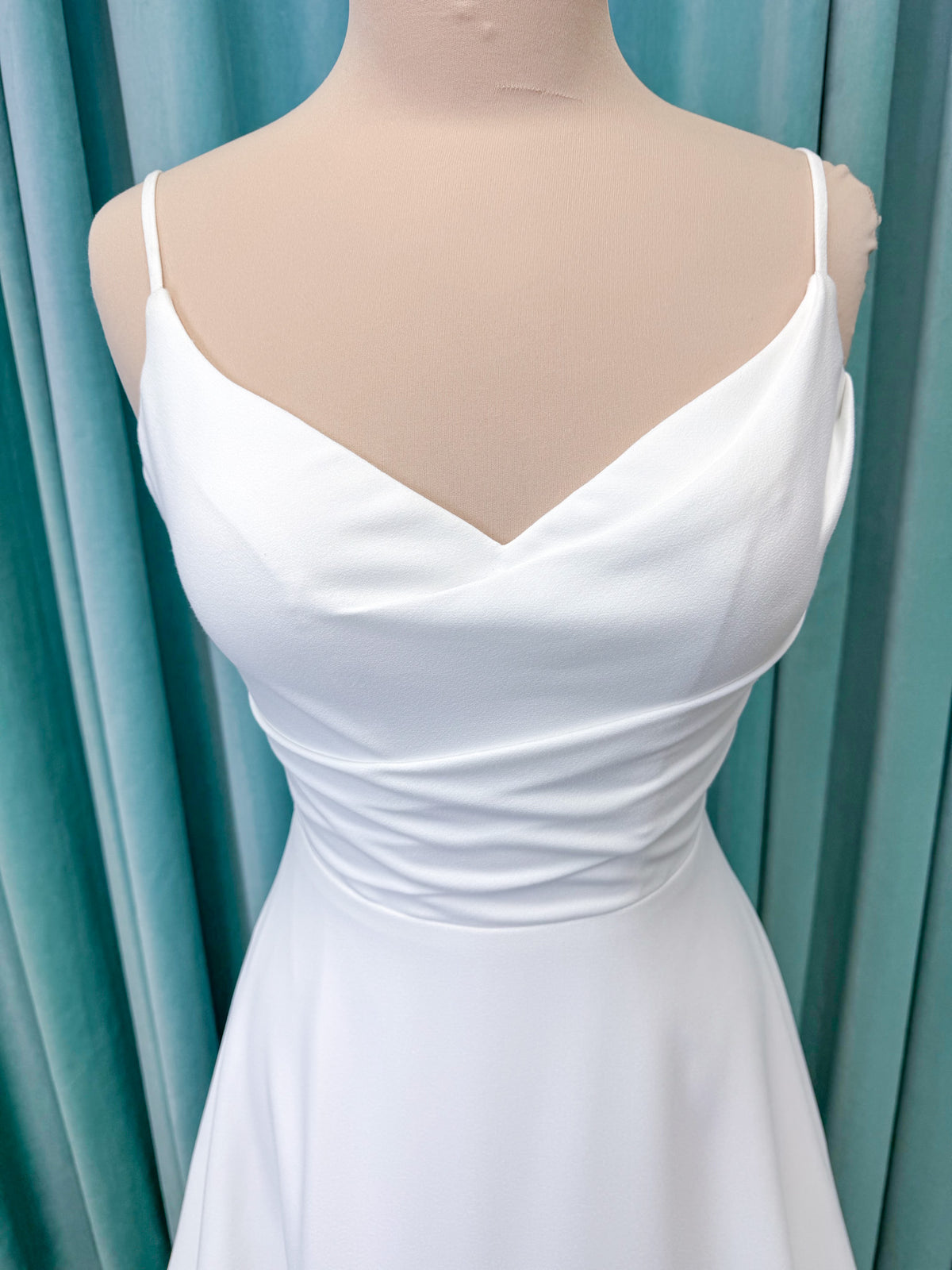 Crepe A-line wedding dress with spaghetti straps, draped V-neckline, ruched bodice, defined waist, and flowing skirt.