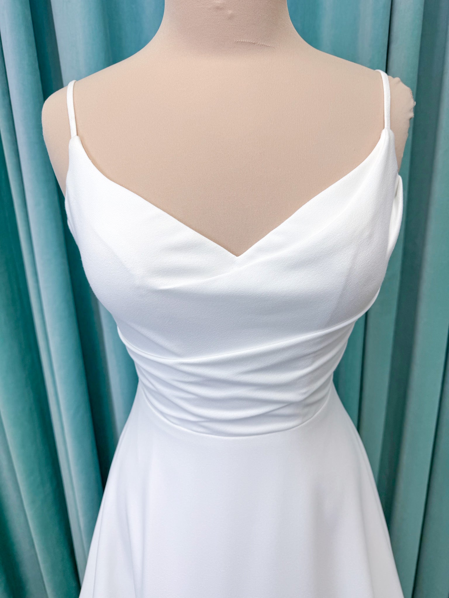 Crepe A-line wedding dress with spaghetti straps, draped V-neckline, ruched bodice, defined waist, and flowing skirt.