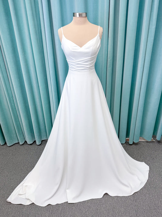 Crepe A-line wedding dress with spaghetti straps, draped V-neckline, ruched bodice, defined waist, and flowing skirt.