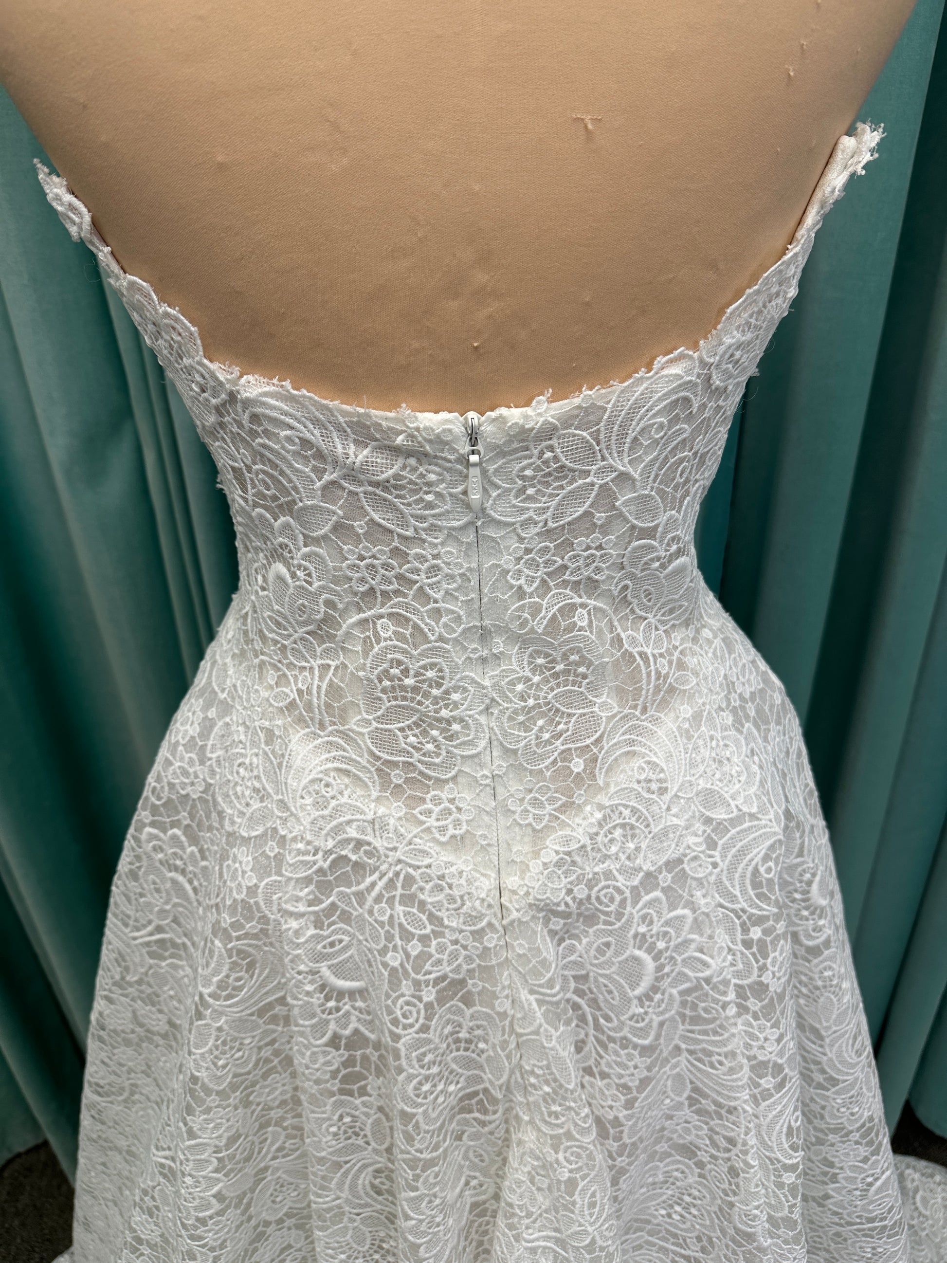 Min ivory strapless sweetheart lace A-line wedding dress on mannequin with illusion corset bodice and voluminous lace skirt.
