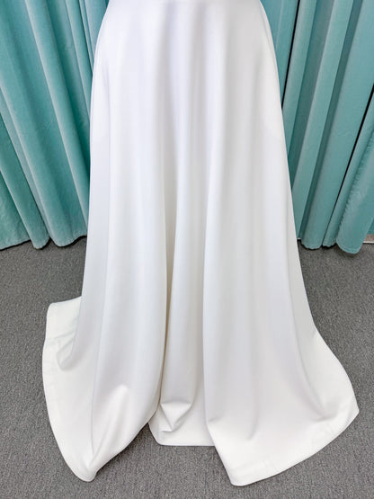 Minimalist crepe A-line wedding dress with spaghetti straps, V-neckline, fitted bodice, natural waist, and flowing skirt.