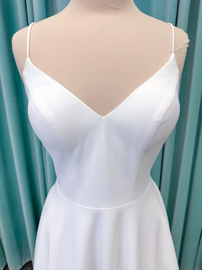 Minimalist crepe A-line wedding dress with spaghetti straps, V-neckline, fitted bodice, natural waist, and flowing skirt.